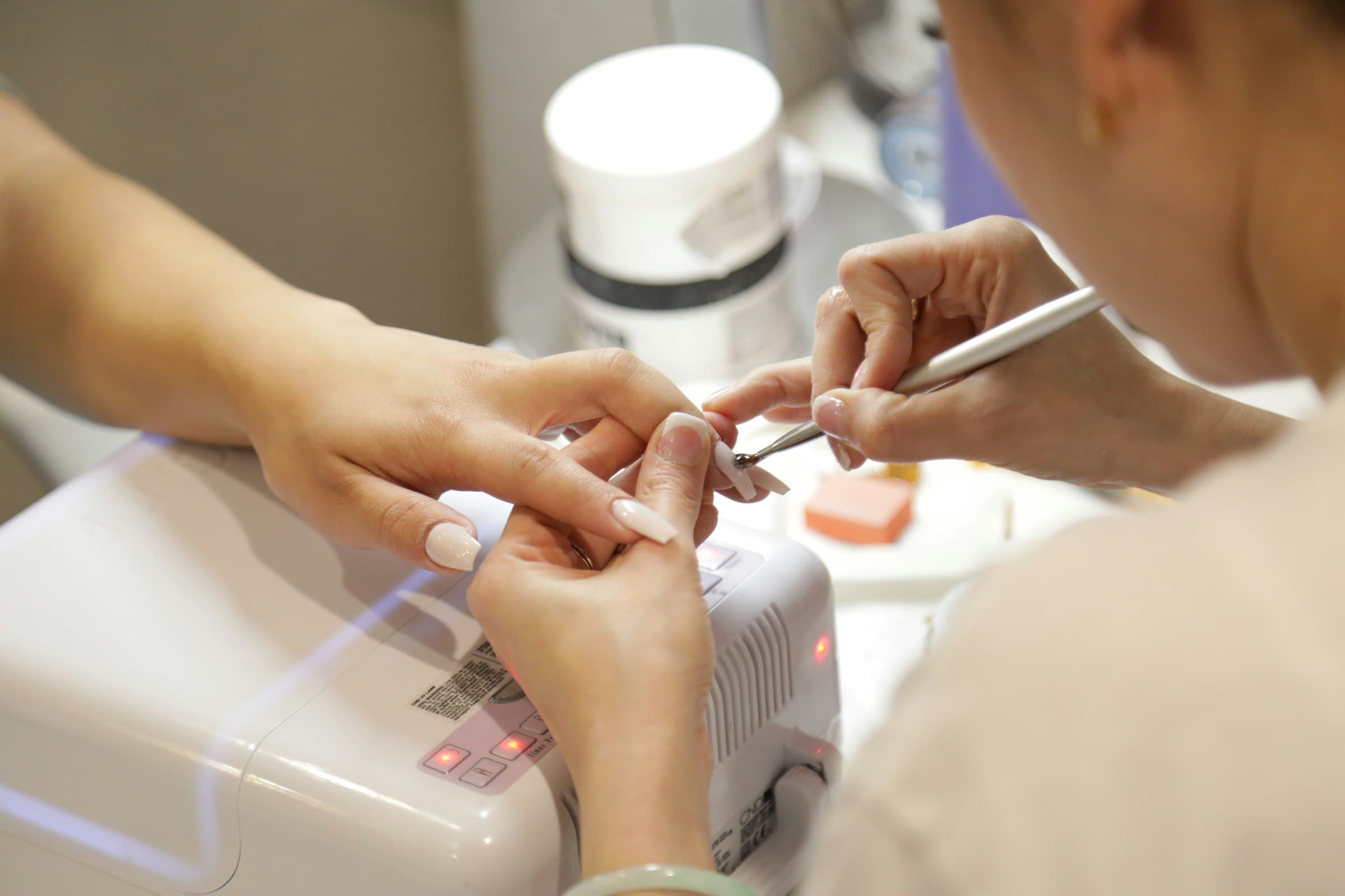 A nail technician shaping a client's nails at a salon station.